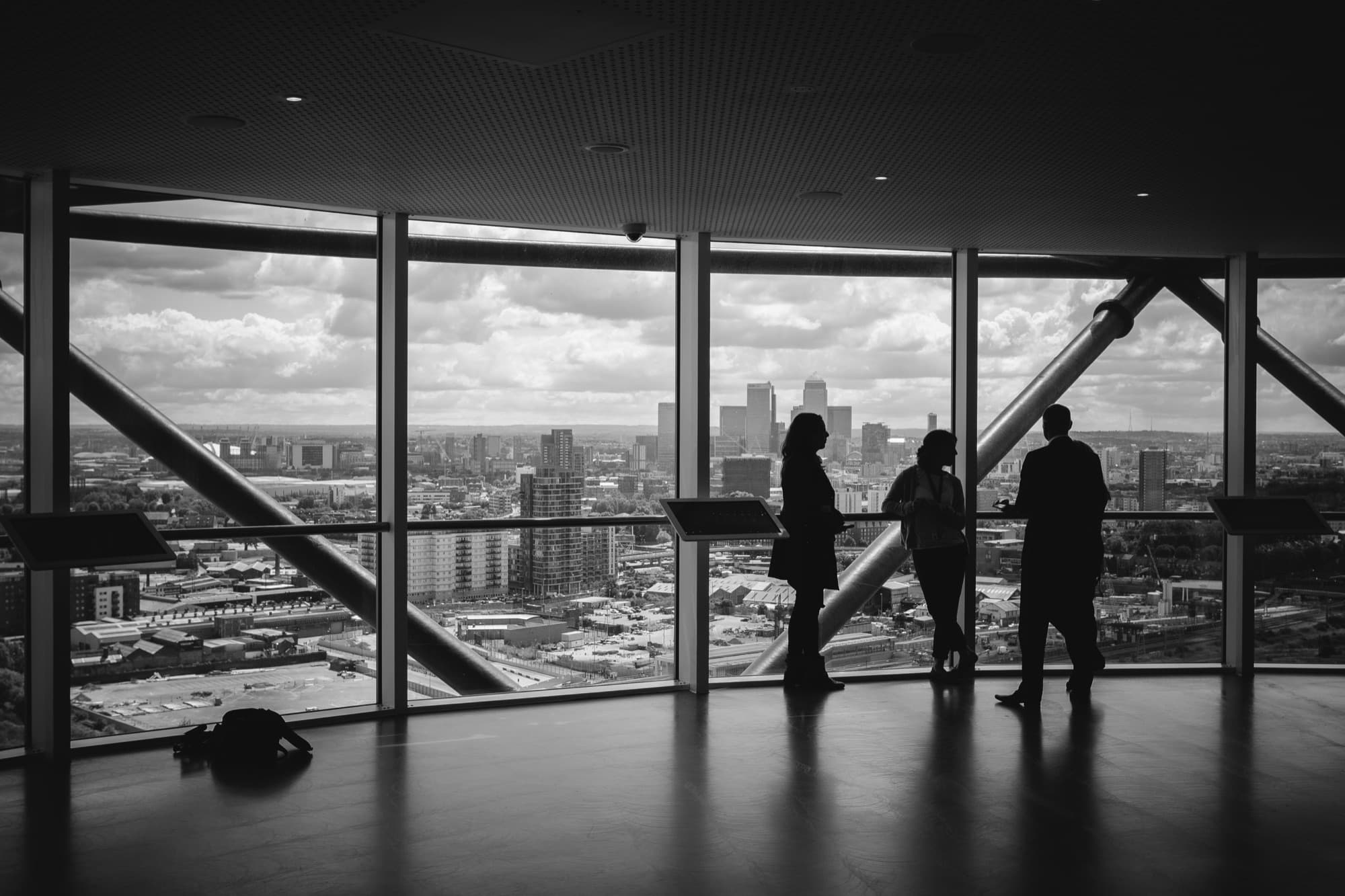 Three professionals in conversation by a floor-to-ceiling window overlooking a city skyline